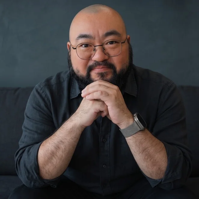 Jason Shew in a dark shirt, sitting on a charcoal sofa
